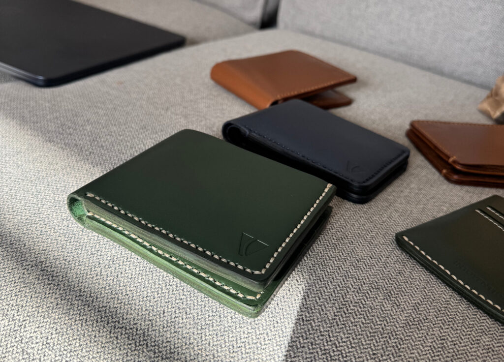 Forest green leather wallet with cream hand stitching in a lifestyle arrangement.