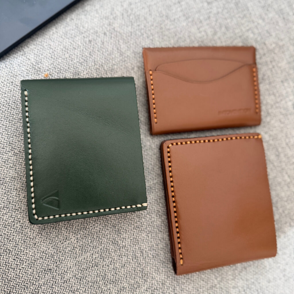 Green and cognac leather goods close-up showing stitching and grain.