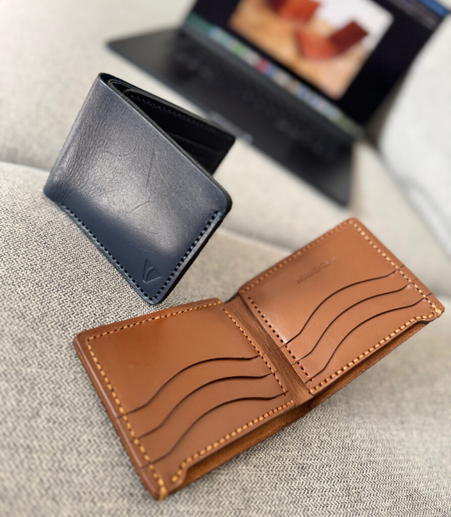 Leather wallets and card holders arranged on a soft grey sofa with a laptop in the background.
