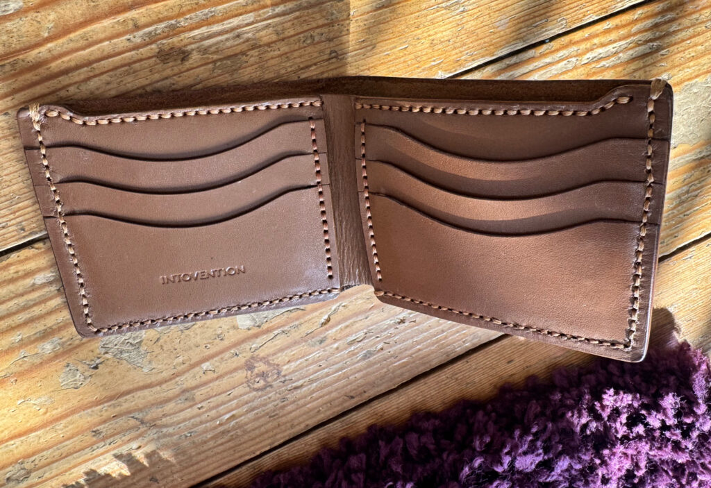 Open brown handmade leather bifold wallet showing interior card slots and hand stitching.